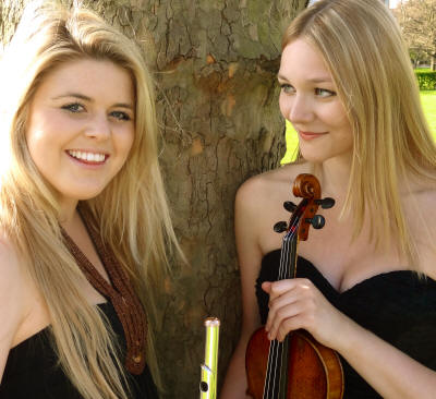 The EG Flute & Violin Duo Duo who play in London , Bedfordshire, & Berkshire, stand next to a tree.