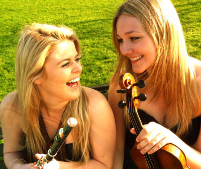 The EG Flute & Violin Duo Laughing string duo rest on grass. They play in Surrey, Sussex & Cambridge